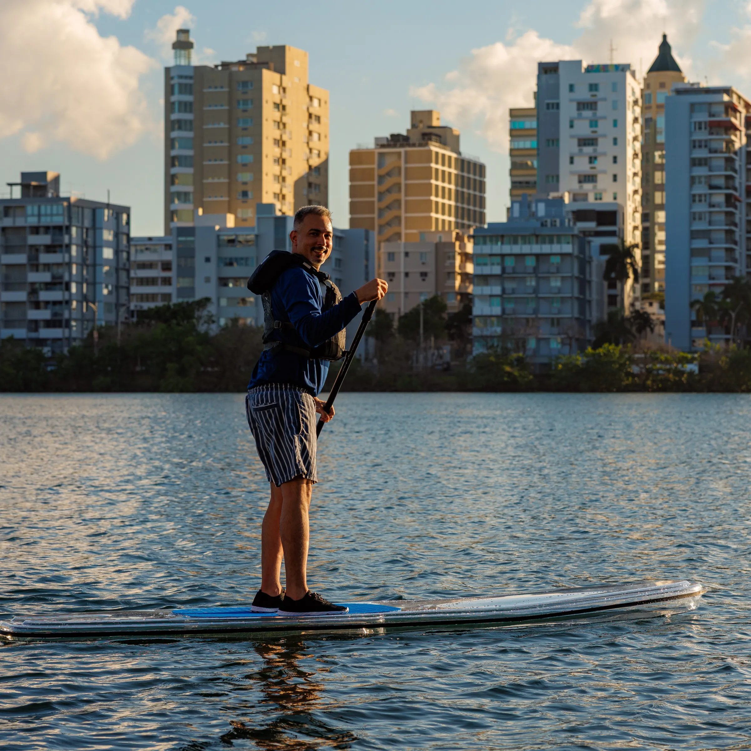 Person paddleboarding on a lake with city buildings in the background.