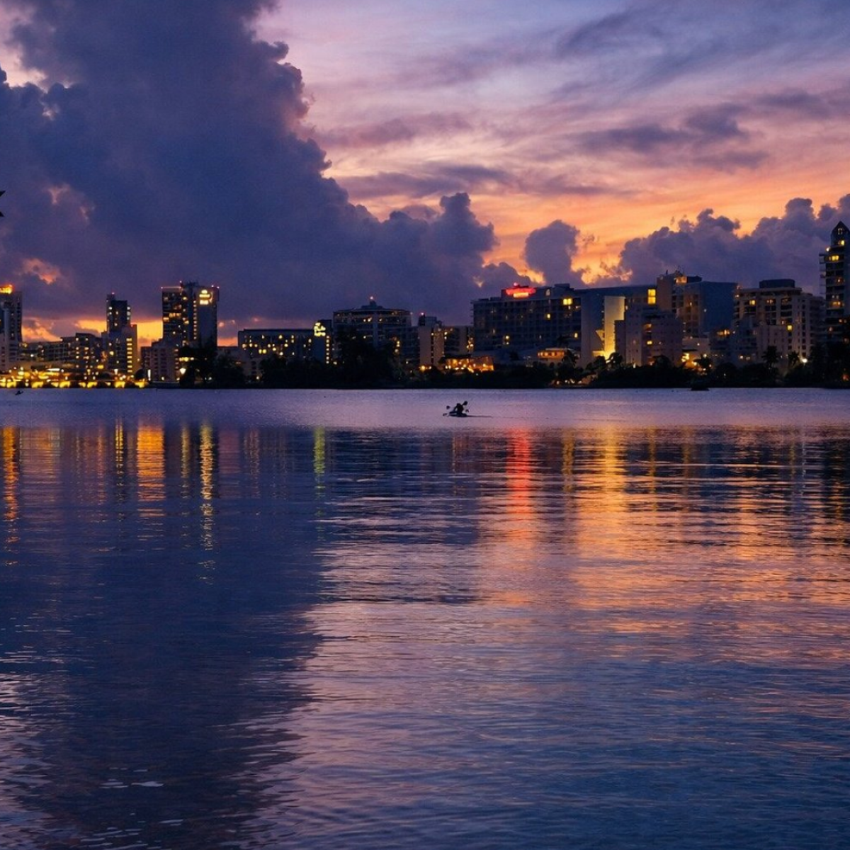 City skyline at dusk with reflections on the water and a cloudy sky.